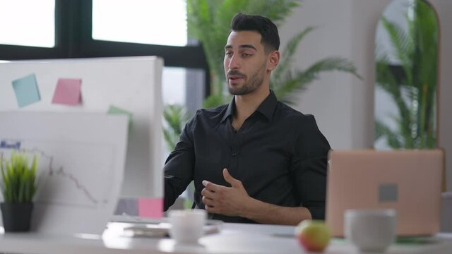 Serious professional Middle Eastern man gesturing talking at computer web camera. Portrait of confident handsome young financial advisor using virtual conferencing in home office