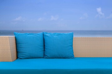 Long brown wicker sofa and blue cushions and cushions placed on the beach - obrazy, fototapety, plakaty
