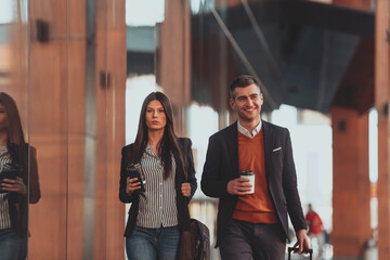 Business man and business woman talking and holding luggage traveling on a business trip, carrying fresh coffee in their hands.Business concept