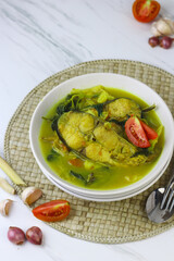 Pindang Ikan Patin or Catfish vegetables Soup , Indonesian food popular from Palembang. Served on ceramic bowl garnished with tomato slices. White marble background.
