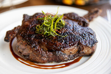 Gourmet ribeye steak dinner grilled to perfection and topped with fresh garnish, drizzled with a reduced sauce. 
