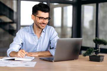 Online education. Intelligent successful caucasian man with glasses, sitting at the workplace,...