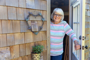 Friendly mature woman with white hair standing at the front door of her home