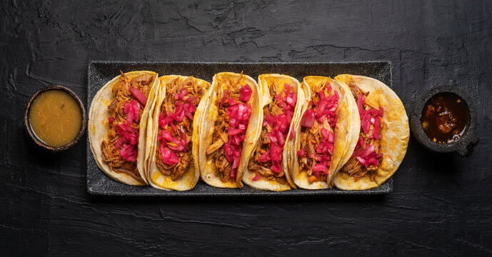 Pork tacos called cochinita pibil with purple onion on dark background. Mexican tacos