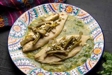 Drowned tlacoyos in green sauce with nopales on dark background. Mexican food