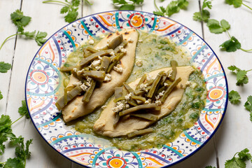 Drowned tlacoyos in green sauce with nopales on white background. Mexican food