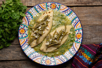 Drowned tlacoyos in green sauce with nopales on wooden background. Mexican food