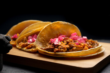 Pork tacos called cochinita pibil with purple onion on dark background. Mexican tacos