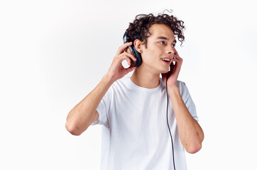 emotional guy with curly hair in headphones listens to music on a light background