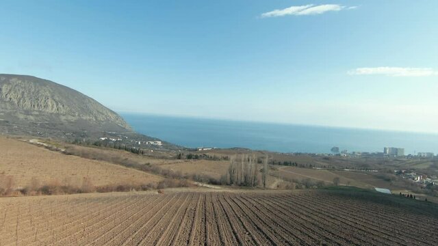 Aerial natural landscape of a hilly region and beautiful blue sea on a summer sunny day. Shot. Flying above green hills and agriculture fields towards the sea.