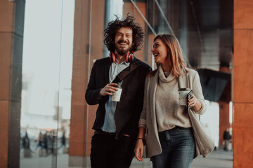 two people on a break from work walk in front of a modern company where they work and drink coffee.