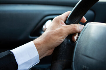 Close up Of A Man Hands Holding Steering Wheel While Driving Car. Businessman while driving, cropped. Driver's hand on steering wheel in suit. Guy sits in car and holds hands on steering wheel