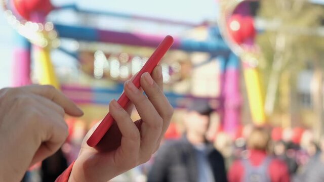 View of female hand holding and pressing on smartphone in the amusement park.