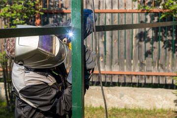 Man welder in welding mask, building uniform and  protective gloves brews metal welding machine on...