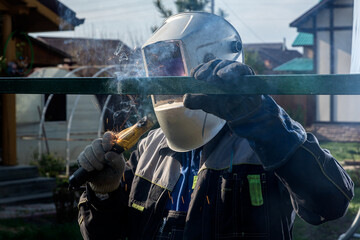 Close up of the a welder welds a fence on the construction site in the village. Construction on a...