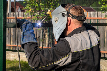 A strong man is a welder in a welding mask and welders leathers, a metal product is welded with a...
