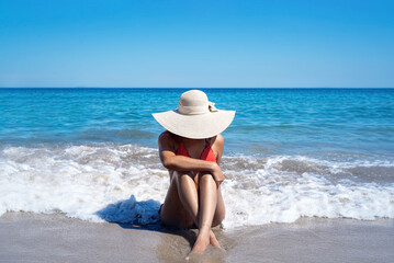 Fototapeta na wymiar Mulher morena de chapéu sentada na areia da praia com ondas