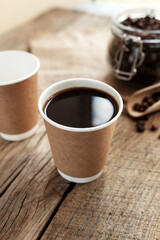 Paper cups of coffee, dry coffee beans in glass jar and spoon at wooden table