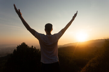 Fototapeta na wymiar Silhouette of young man raises his hands up to sunset or sunrise on on top of hill in the summer 