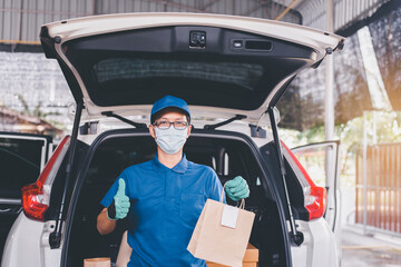 Delivery asian man employee wearing face mask standing and holding paper bag in front of van during coronavirus pandemic situation