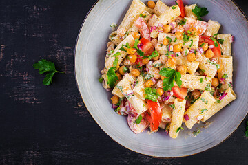 Vegetarian vegetable pasta. Pasta rigatoni with tomato, red onion, parsley and fried chickpeas with nut sauce. Vegan food. Top view, overhead