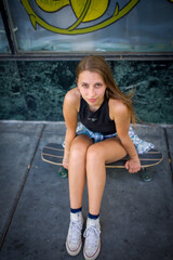 Naklejka premium Down Angle Portrait of Teenage Girl Seated on Skateboard in San Jose