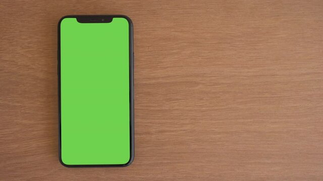 Smart phone place on wood table, Green screen telephone, Close up display mobile phone with mock up, Chroma key monitor, Close-up the cell phone on brown desktop, Mockup smartphone, Zoom top view.
