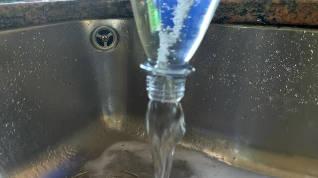 Slow motion shot of pouring circling water out of bottle into sink,close up