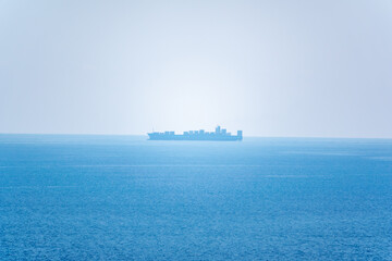 Calm blue sea with the silhouette of a large ship on the horizon