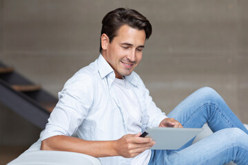 Handsome smiling man with digital tablet on sofa at home, online shopping