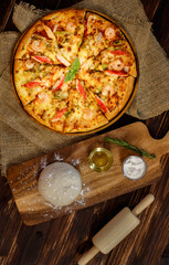 Close up on dough, olive oil, powder and rolling pin for making homemade seafood pizza with shrimp, crab sticks, bell peppers on sackcloth and wooden table. Food Concept.