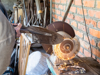 gardener sharpens shovel on electric grinder