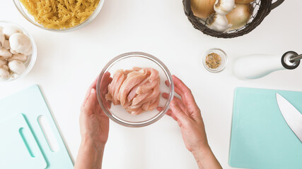 Bowl of raw chopped chicken fillet close up on white kitchen table. Pasta with mushrooms and chicken recipe, preparation process
