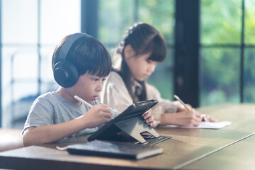 Asian homeschool boy and girl learning online at home by using tablet.