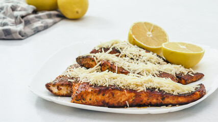 Smoked paprika roasted salmon served with Parmesan cheese and lemon slices close up on a plate.