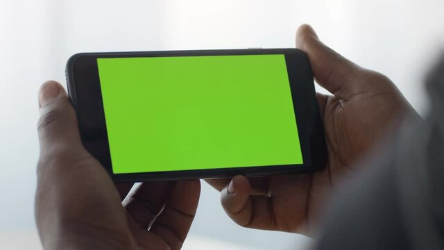 Mobile tv. Close up shot of smartphone with green chroma key screen in black male hands, man watching videos online