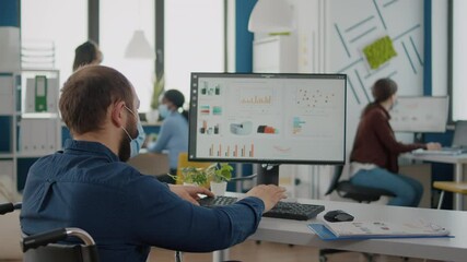 Immobilized business man with protective mask working in new normal business financial company typing on pc, checking reports, analysing data looking at desktop sitting in wheelchair - Powered by Adobe