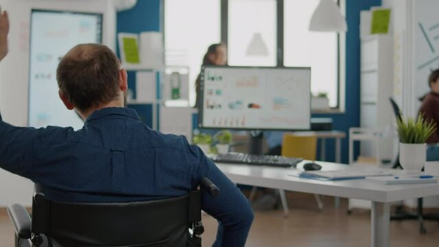 Immobilized disabled paralized independence project manager entering in start up business office with wheelchair greetting diverse colleagues. Multiethnic team working at financial economic project