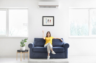 Young woman with air conditioner remote control at home