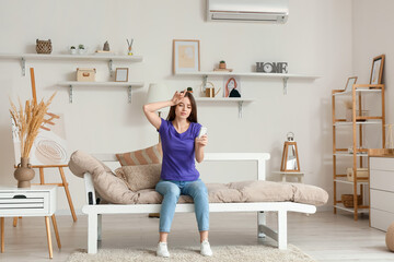 Young woman with air conditioner remote control sitting on sofa in living room