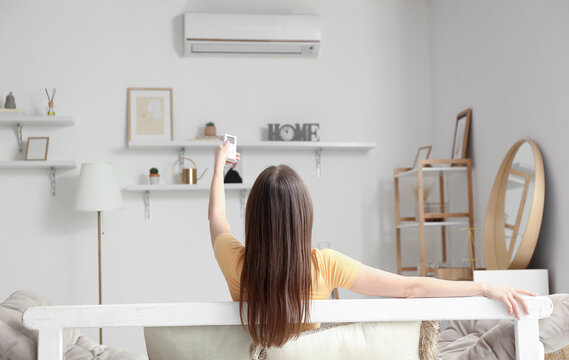 Young woman with air conditioner remote control on sofa at home