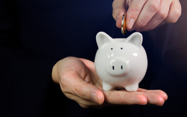 Young businesswoman putting a piggy bank on hand Dropping money into savings, wealth, riches...