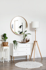 Interior of stylish room with mirror, lamp and chest of drawers