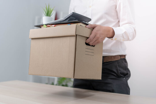 A businessman holds a box for personal items after sending a resignation letter to an executive or manager. Include information about resignation and vacancies and job changes.