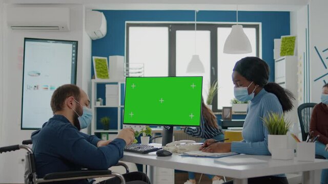 Handicapped paralysed invalid entretreneur with face mask explaning to black employee financial evolution of company pointing at green screen, mock up, chroma key izolated desktop in new normal office