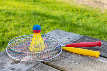 Badminton game rackets and shuttlecock on wooden table with green grass in the park on a sunny summer day.