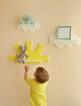Stylish and modern Interior design. Home for the child room. todder boy takes a gray hare's soft toy from the shelf.