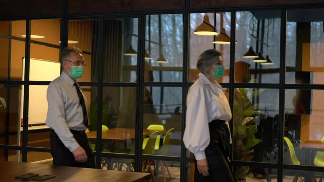 Side view of corporate directors in disposable masks walking to briefing  meeting with social distance in 1m, experienced business partners during working day in office at pandemic quarantine
