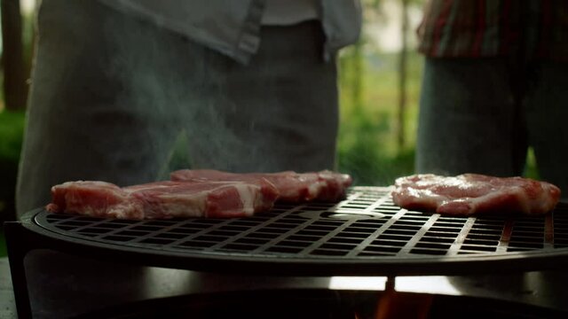 Chef putting meat slices on grate outside. Man cooking meat on grille outdoors