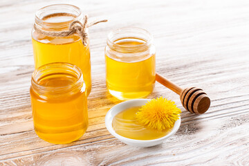 Flower honey in a glass jar and dandelions on a table